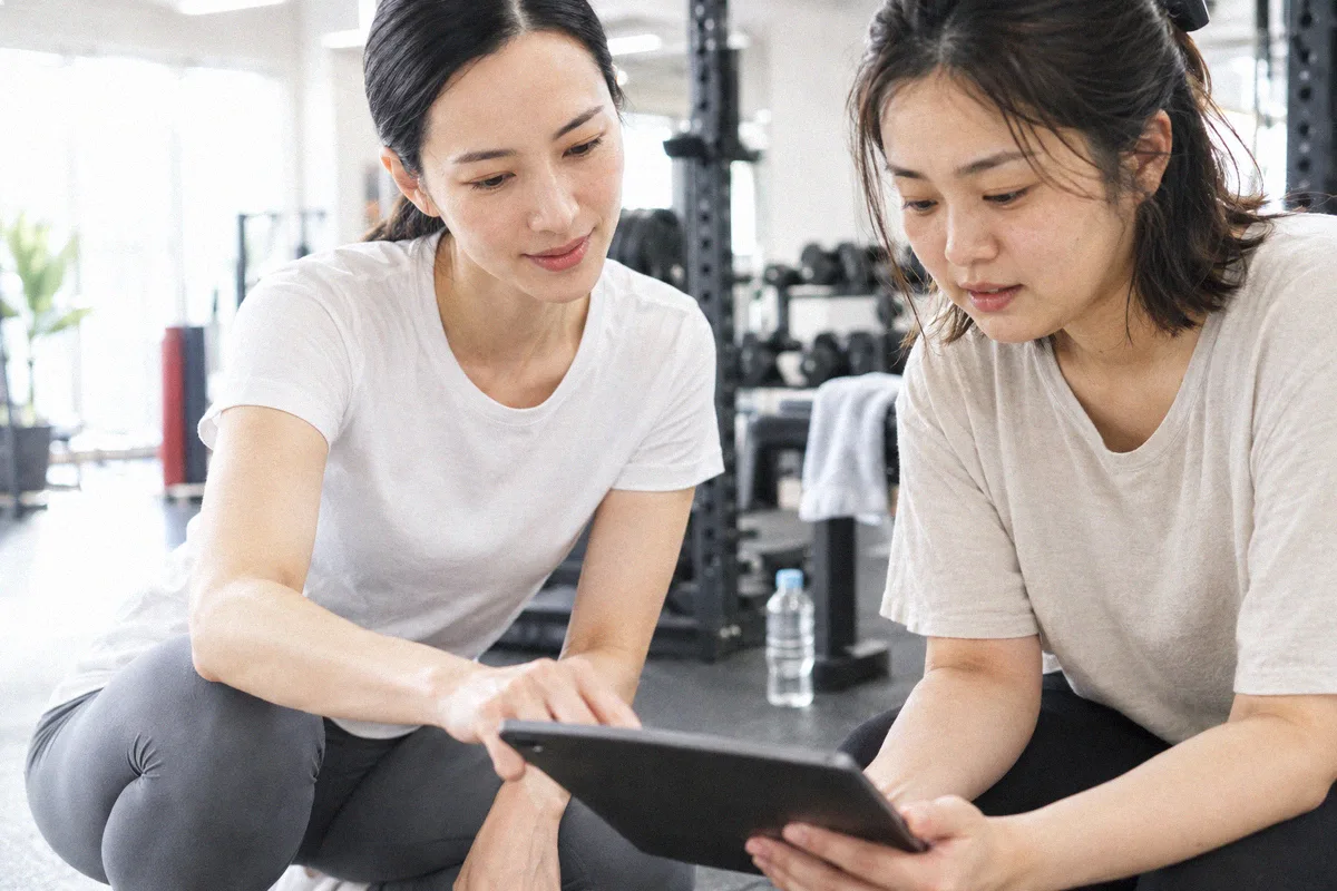 座った利用者の横にかがみ、タブレットの画面を一緒に見るトレーナー