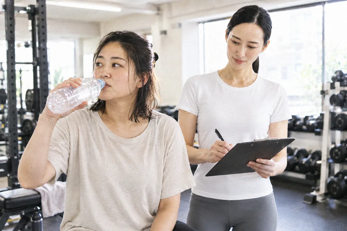 セットの合間に水分を取る利用者と、次の種目を確認するトレーナー
