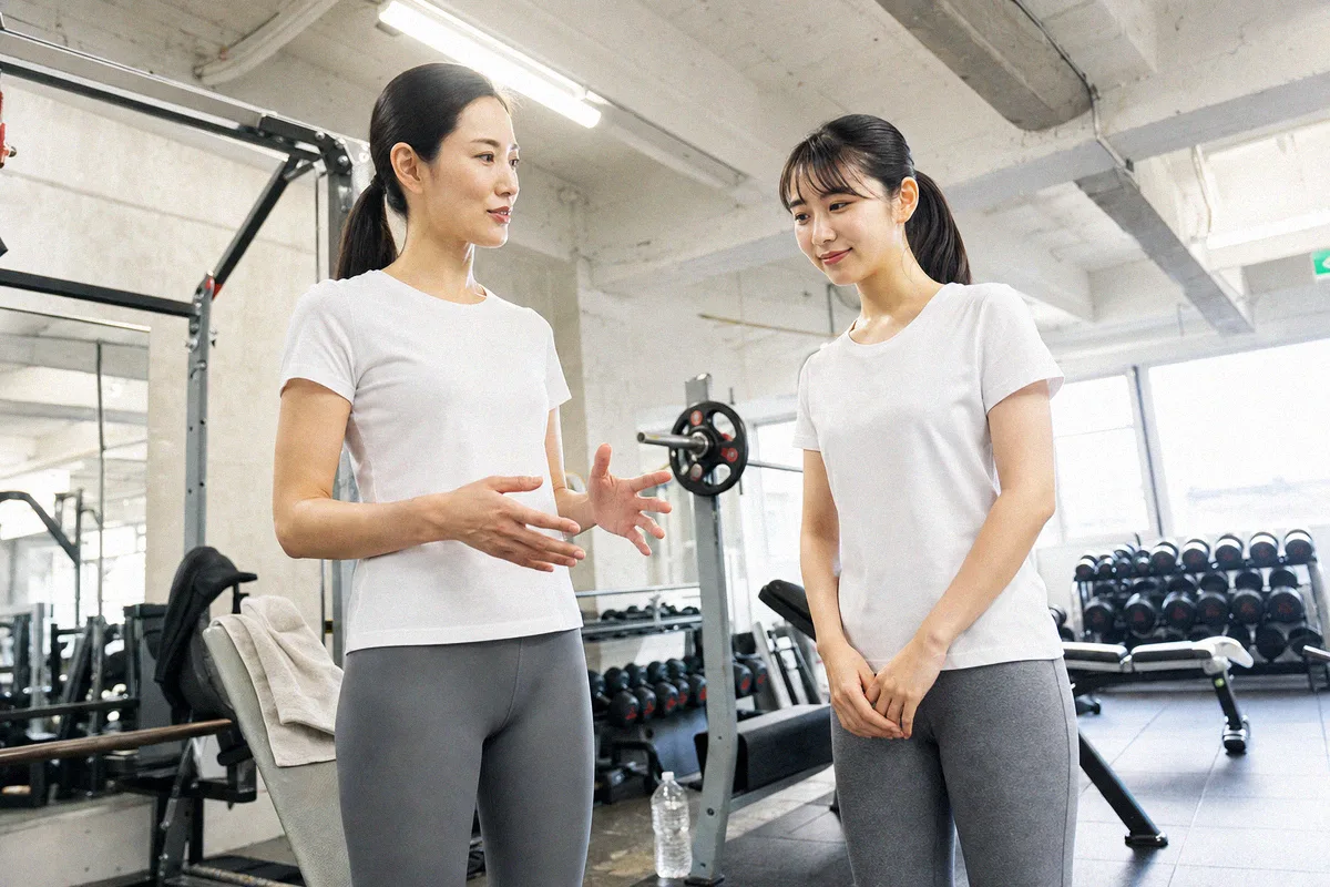 器具の前で手ぶりを交えて説明するトレーナーと、聞く利用者