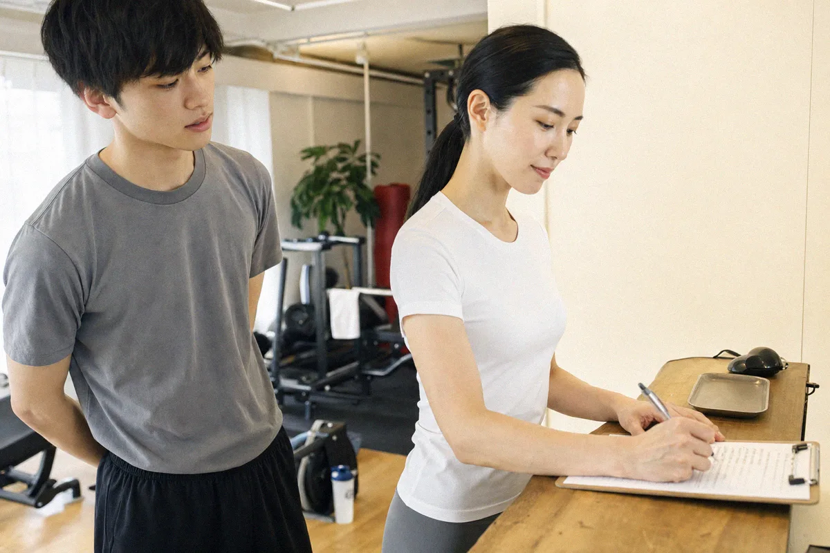 スタジオの入口で初回の流れを説明するトレーナーと利用者