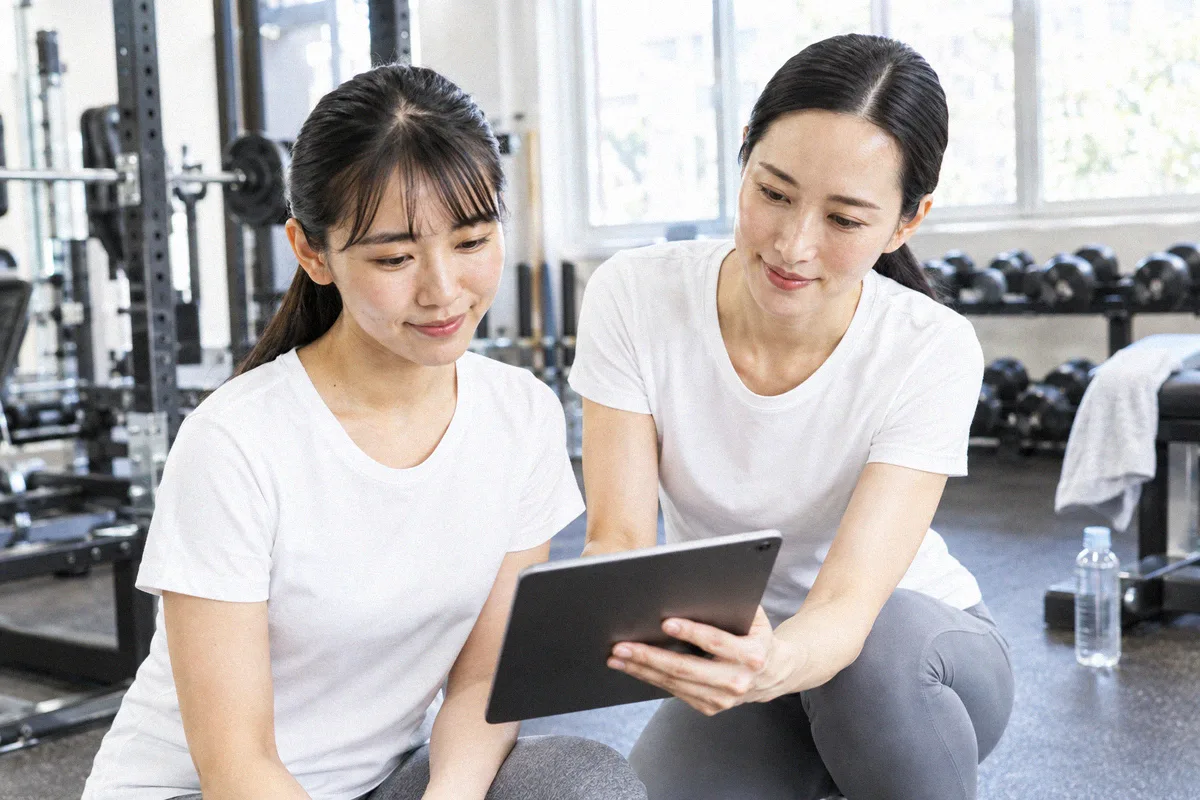 座った利用者の横にかがみ、タブレットの画面を一緒に見るトレーナー