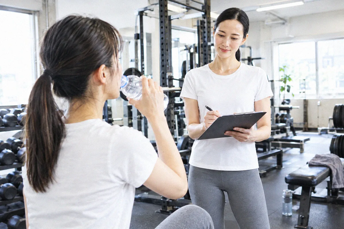 セットの合間に水分を取る利用者と、次の種目を確認するトレーナー