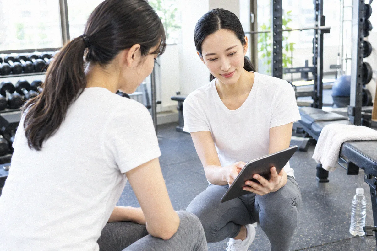 座った利用者の横にかがみ、タブレットの画面を一緒に見るトレーナー