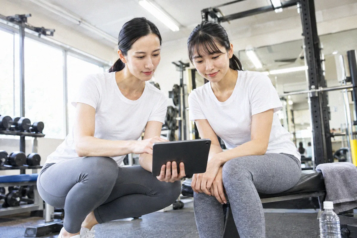 座った利用者の横にかがみ、タブレットの画面を一緒に見るトレーナー