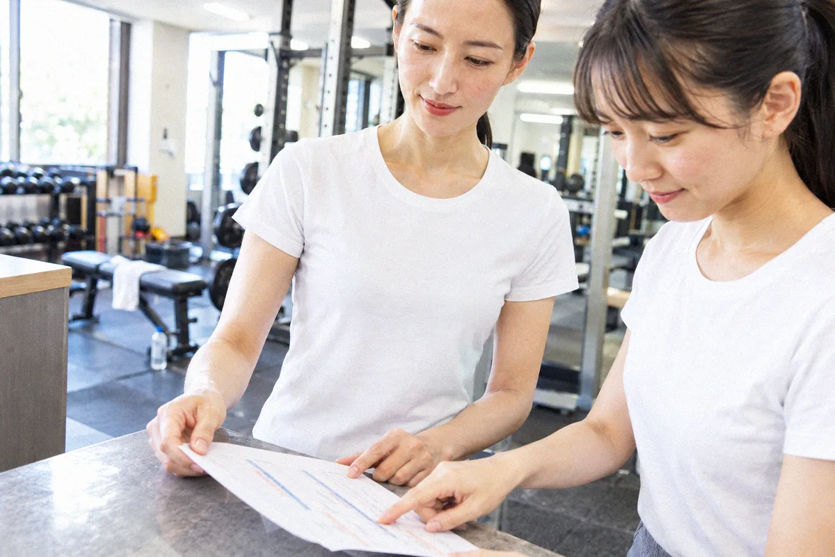受付カウンターで印刷したプランを指しながら確認する利用者とトレーナー